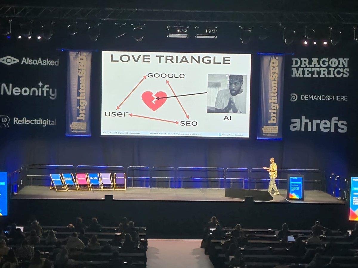 Akash Hashmi on the main stage at Brighton SEO, presenting a 'Love Triangle' slide about Google, users, SEO and AI